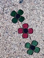 A decorative glass piece featuring a chain of daisy shapes in green and pink colors on a textured background.