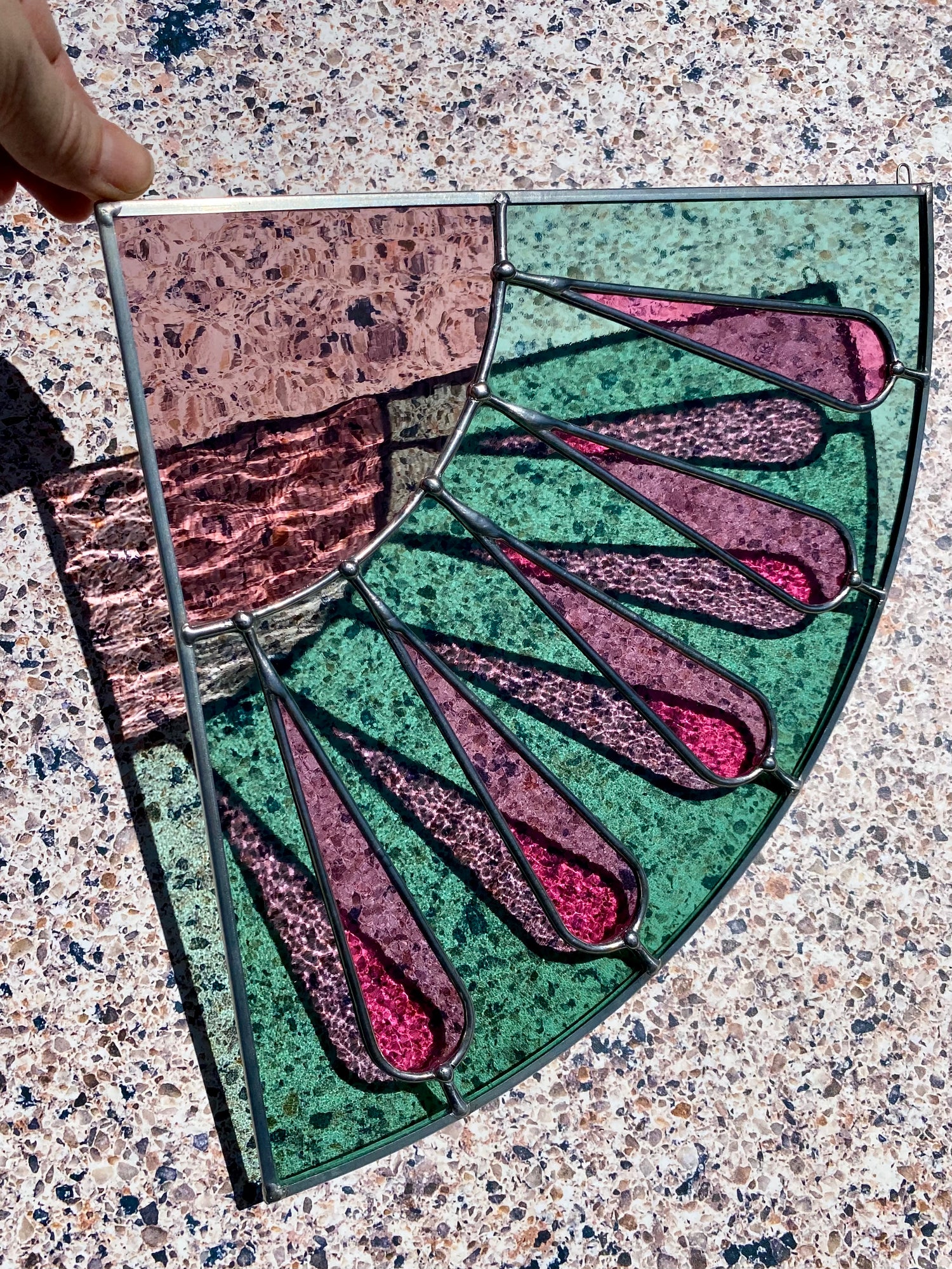 A stained glass corner panel with a sunburst pattern, featuring a watermelon colorway, on a textured background