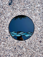 A stained glass mirror with a unique wave design against a textured surface