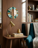 Decorative mirror with colorful tiles on a wooden wall above a side table with a lamp and books.