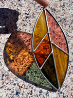 Stained glass leaf with multicolored shades held over a speckled surface