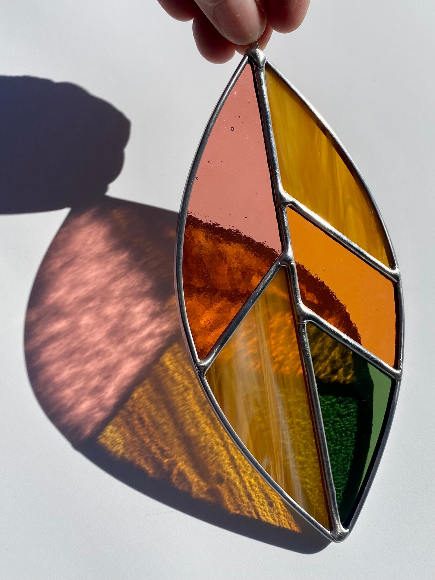 Stained glass leaf-shaped panel held by a hand against a white background