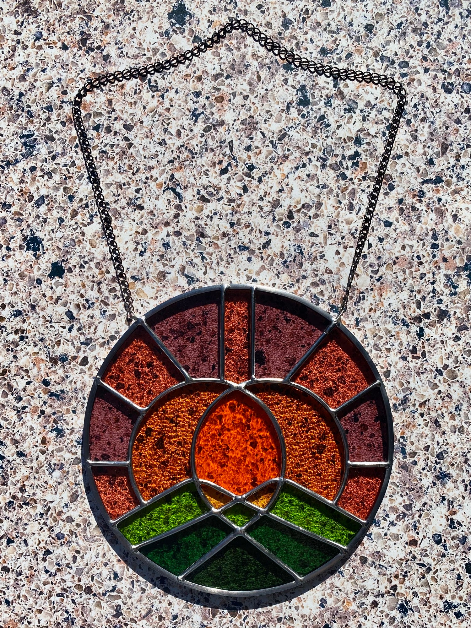 Round stained glass panel with landscape design on a textured surface