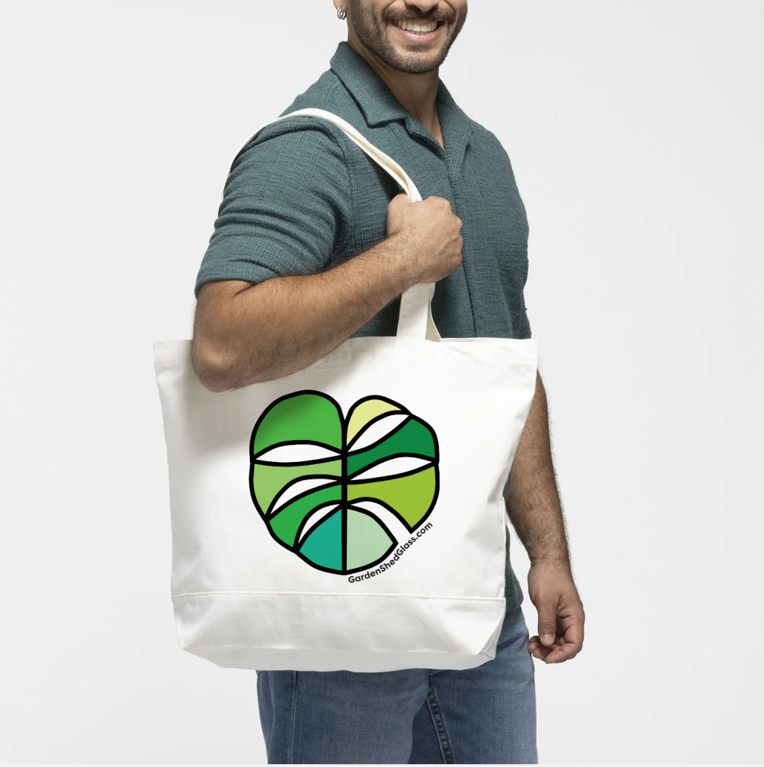 Man holding a white tote bag with a green and white monstera logo on a white background