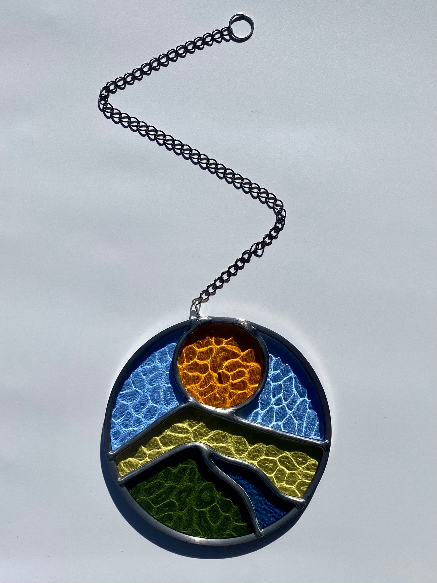 Round stained glass sun catcher with a landscape design against a white background