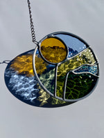 Round stained glass sun catcher with a landscape design against a white background