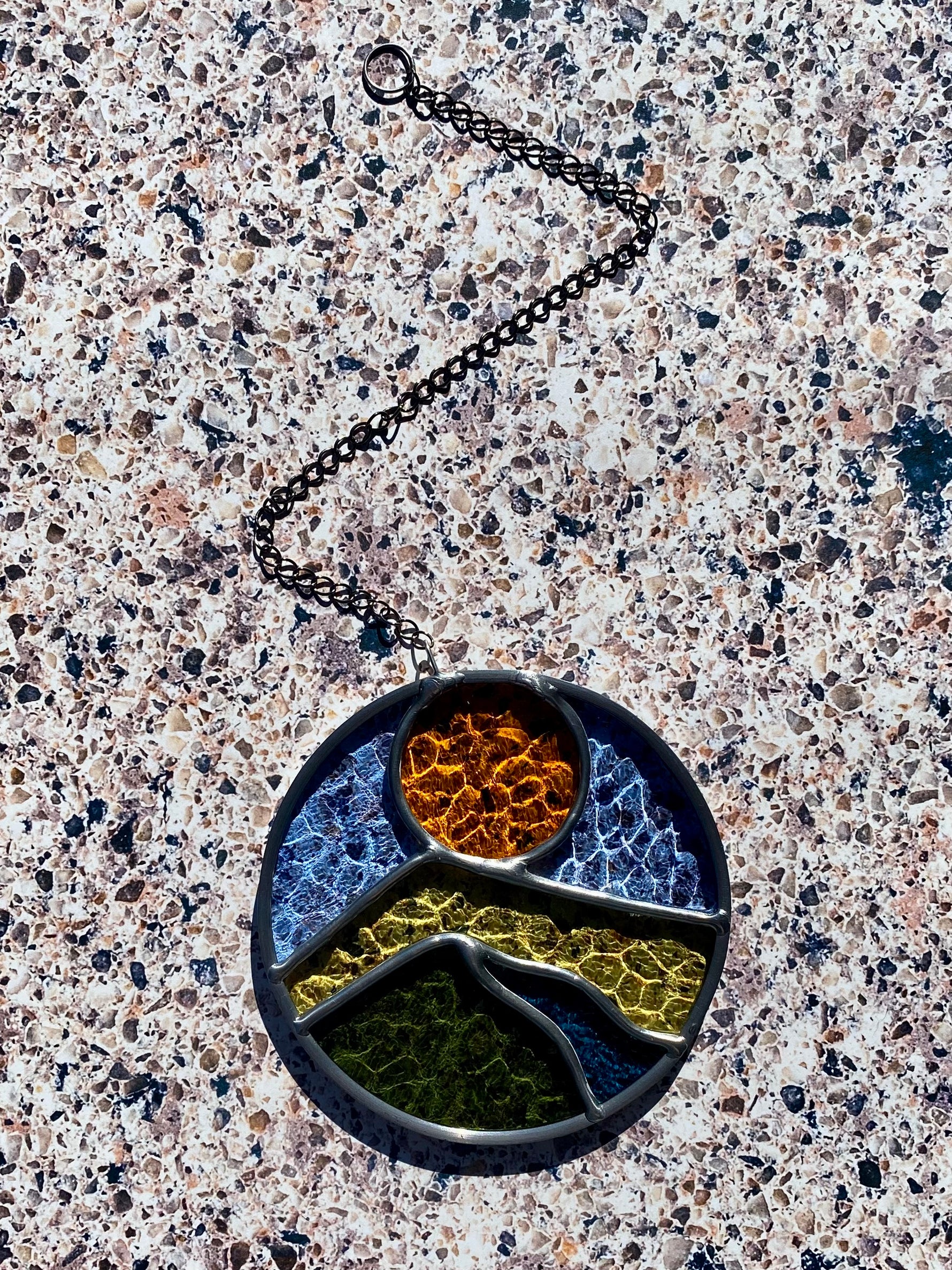 Round stained glass sun catcher with a landscape design against a textured background