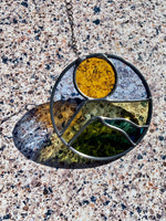 Round stained glass sun catcher with a landscape design against a textured background