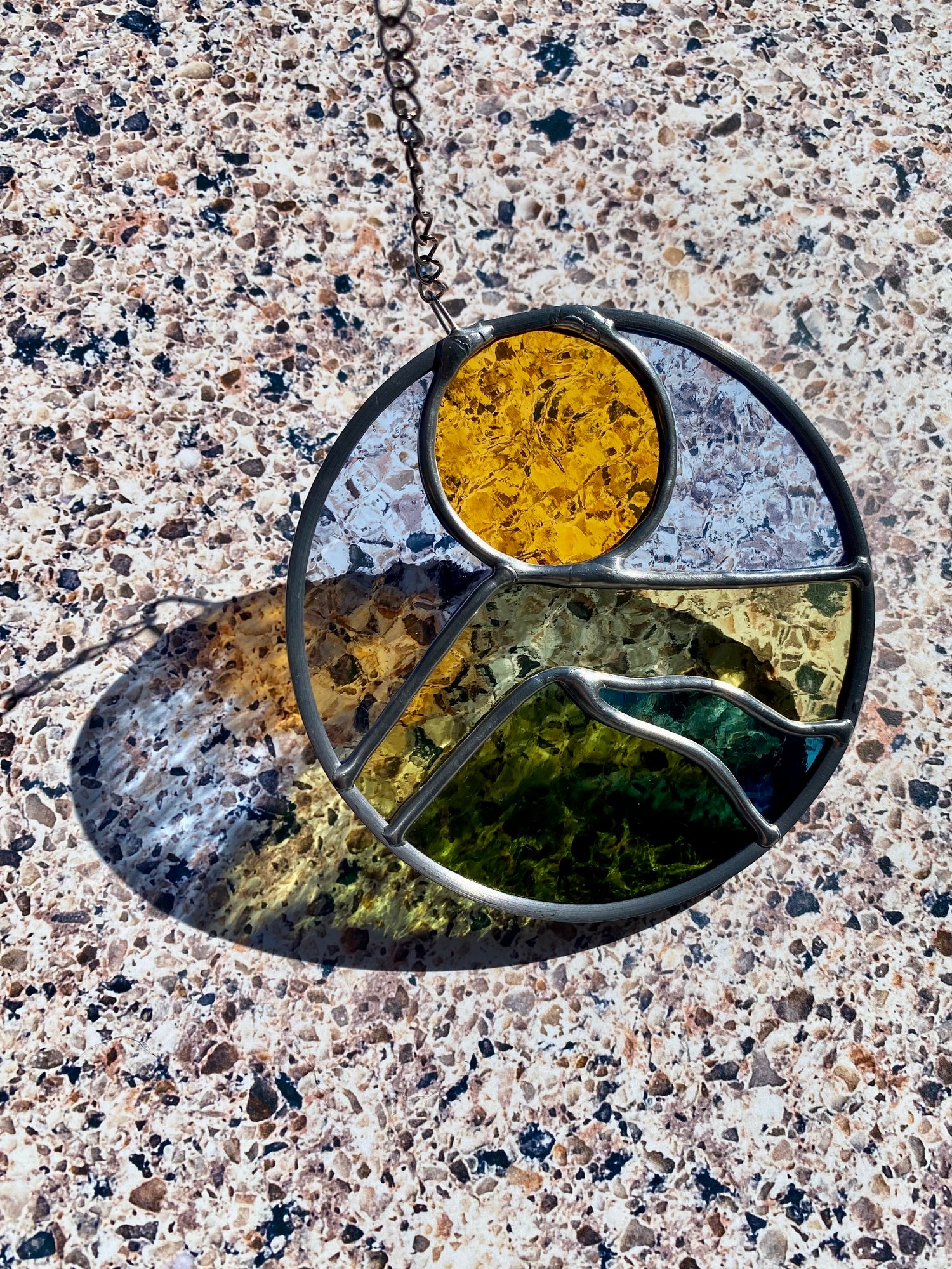Round stained glass sun catcher with a landscape design against a textured background