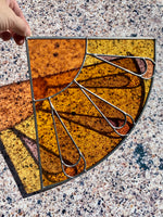 Decorative stained glass corner panel with a sunburst design on a textured surface
