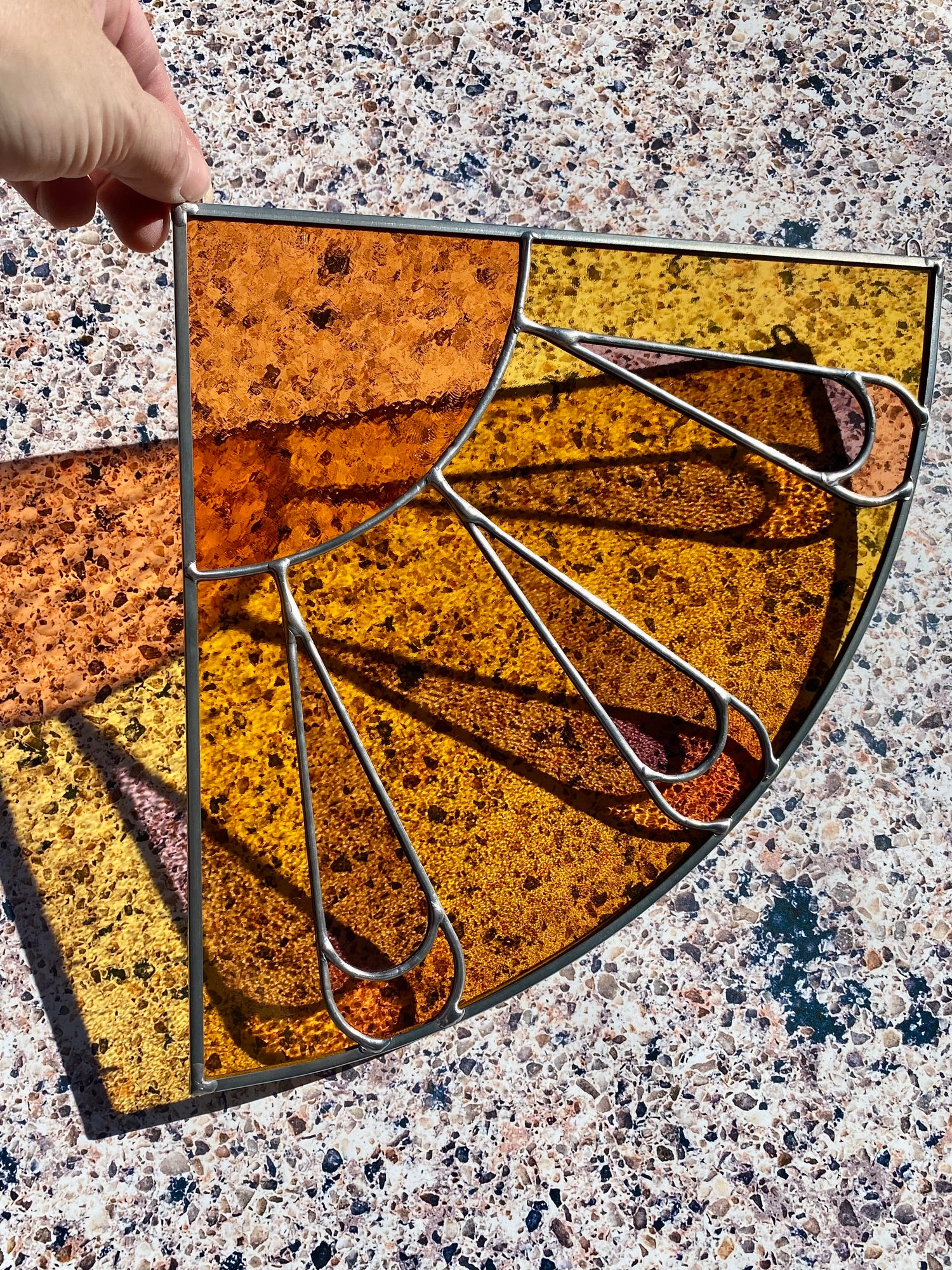 Decorative stained glass corner panel with a sunburst design on a textured surface