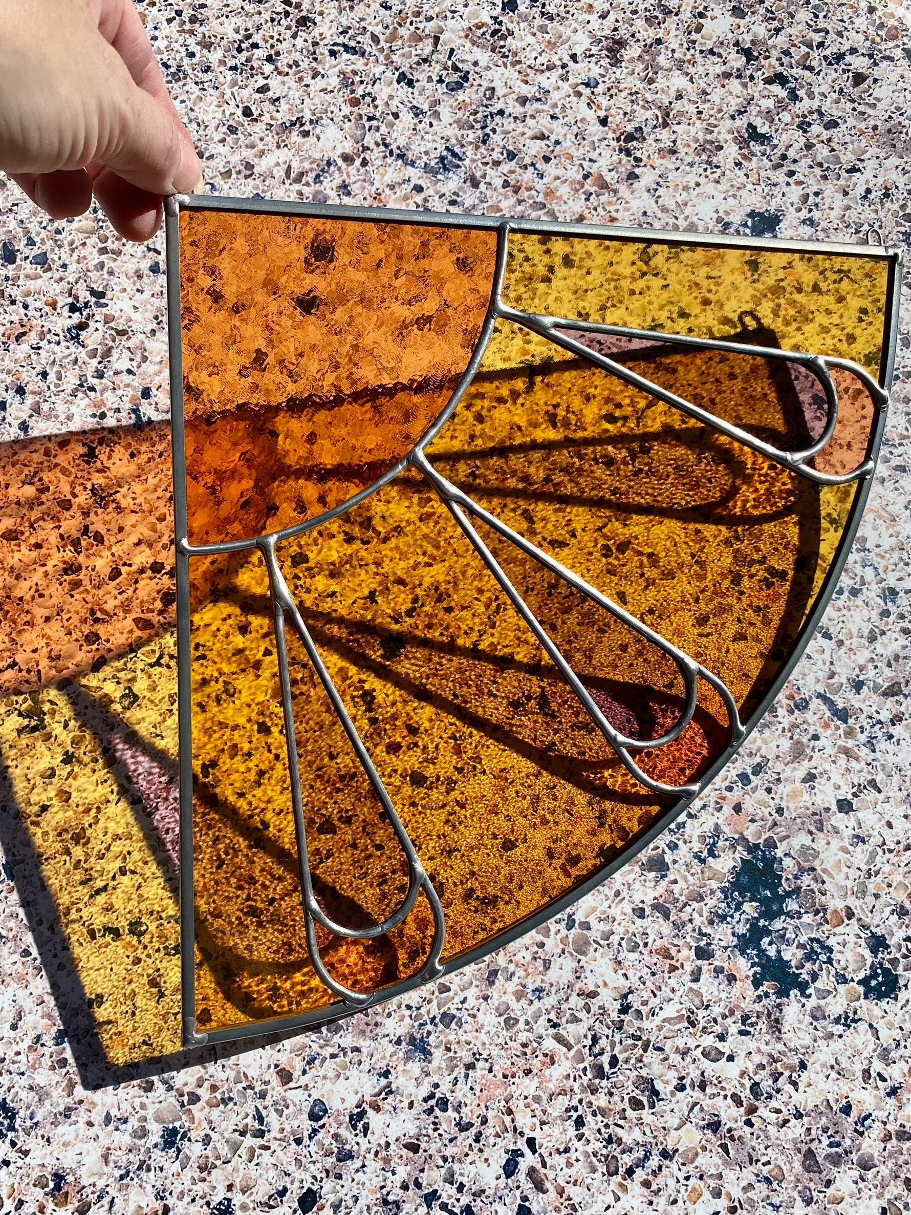 Decorative stained glass corner panel with a sunburst design on a textured surface