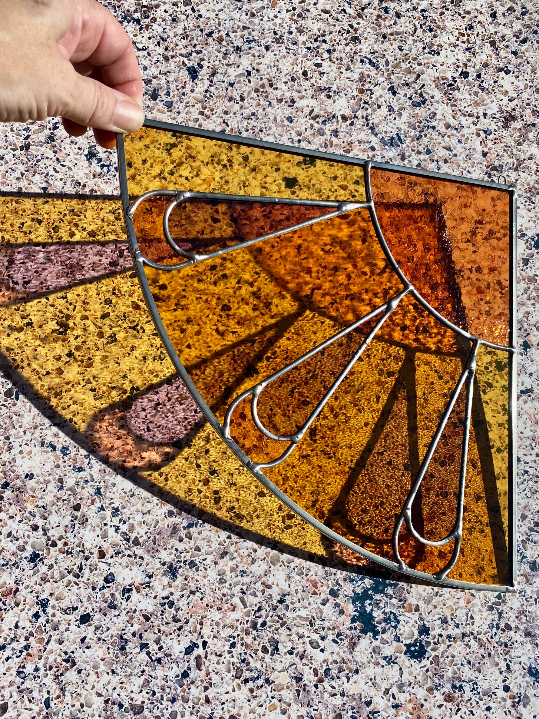 Decorative stained glass corner panel with a sunburst design on a textured surface